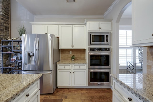 kitchen featuring white cabinets, backsplash, stainless steel appliances, crown molding, and light stone countertops