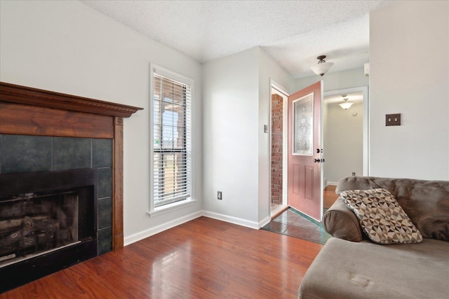 living room with hardwood / wood-style flooring, a tiled fireplace, and a textured ceiling