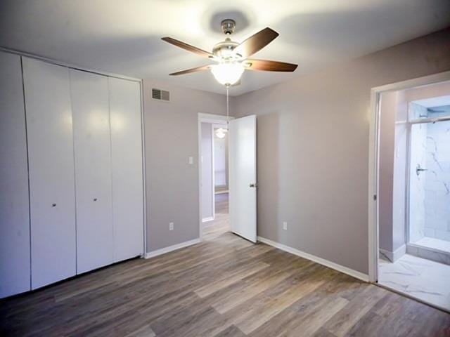 unfurnished bedroom with hardwood / wood-style flooring, ensuite bathroom, ceiling fan, and a closet