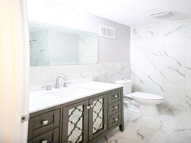 bathroom featuring vanity, toilet, and tile walls