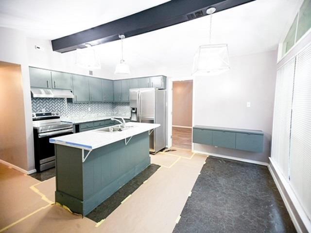 kitchen featuring tasteful backsplash, appliances with stainless steel finishes, a kitchen breakfast bar, beamed ceiling, and a kitchen island with sink