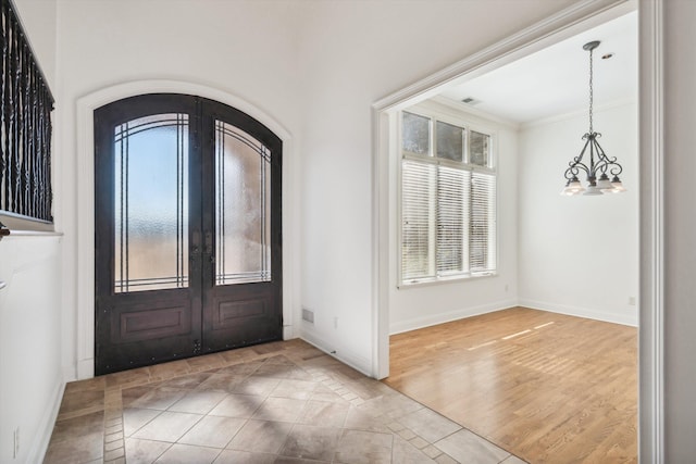 foyer entrance with french doors, ornamental molding, hardwood / wood-style floors, and a notable chandelier