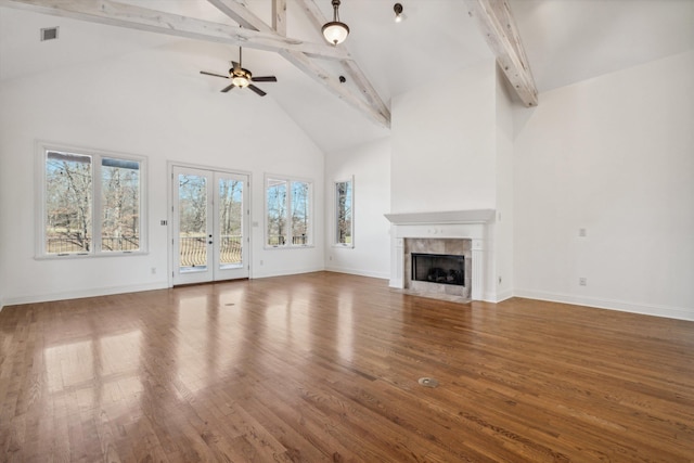 unfurnished living room with hardwood / wood-style flooring, a tile fireplace, ceiling fan, high vaulted ceiling, and beamed ceiling