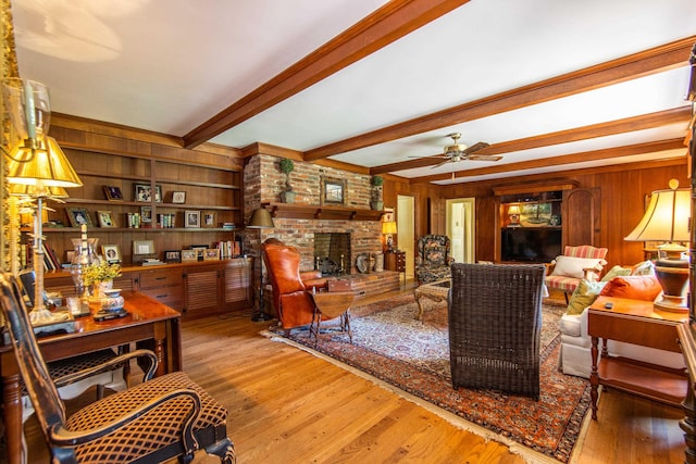 living room with beamed ceiling, wooden walls, hardwood / wood-style flooring, ceiling fan, and a fireplace