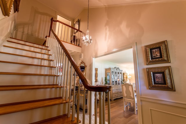 staircase featuring a high ceiling, crown molding, hardwood / wood-style floors, and a notable chandelier