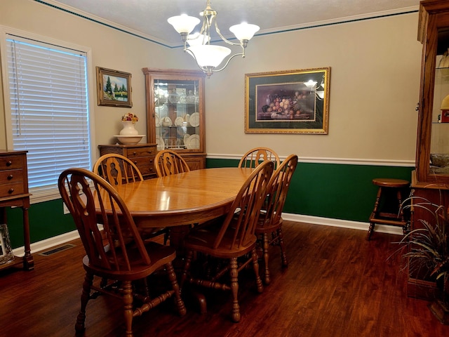 dining space featuring dark wood-type flooring, ornamental molding, and an inviting chandelier