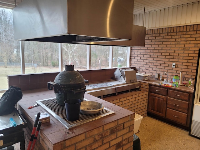 kitchen with brick wall, tile countertops, sink, and wall chimney range hood