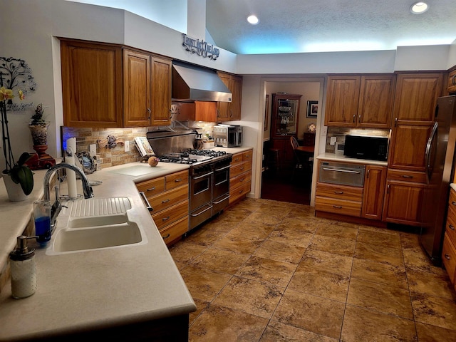 kitchen with wall chimney exhaust hood, sink, range with two ovens, fridge, and decorative backsplash