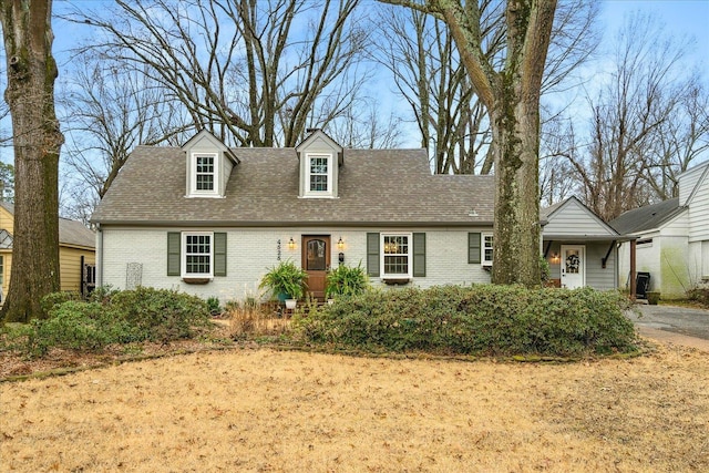 cape cod-style house featuring a shingled roof and brick siding