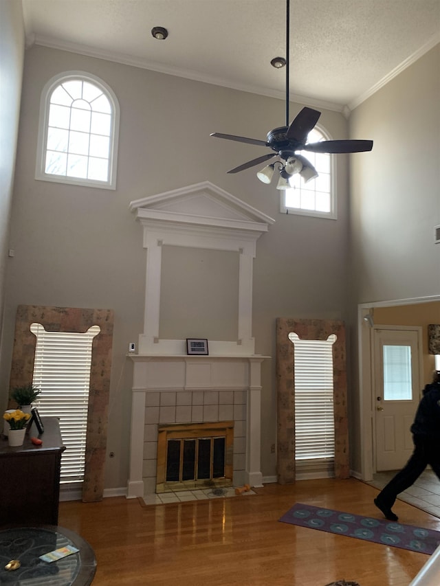 unfurnished living room featuring hardwood / wood-style flooring, ceiling fan, ornamental molding, and a tile fireplace