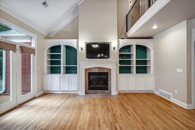 unfurnished living room featuring a tiled fireplace, crown molding, light hardwood / wood-style floors, and built in shelves