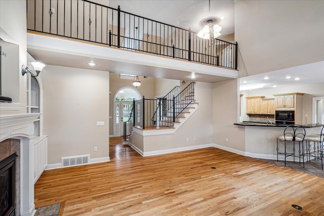 living room featuring a tiled fireplace, a towering ceiling, and light wood-type flooring