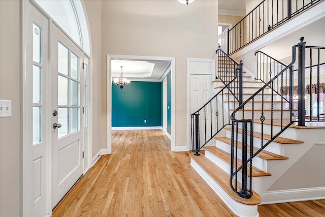 entryway with crown molding, a towering ceiling, wood-type flooring, and a notable chandelier