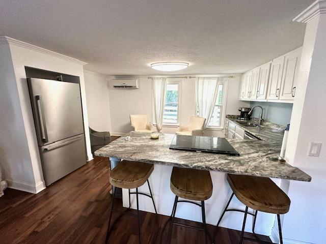 kitchen with white cabinets, stainless steel fridge, kitchen peninsula, light stone countertops, and dark wood-type flooring