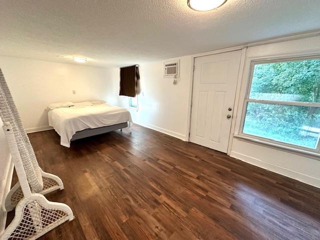 bedroom featuring dark hardwood / wood-style floors, a wall mounted air conditioner, and a textured ceiling