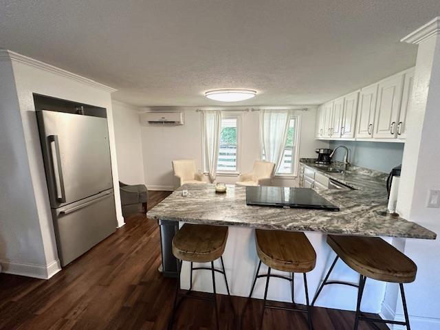 kitchen with dark wood-type flooring, high end fridge, a wall mounted air conditioner, kitchen peninsula, and white cabinets