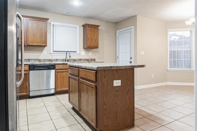 kitchen with appliances with stainless steel finishes, sink, a center island, light tile patterned floors, and a textured ceiling