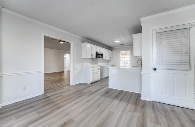 kitchen with white cabinetry, sink, ornamental molding, a textured ceiling, and light hardwood / wood-style flooring