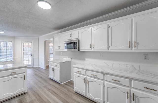 kitchen with white cabinetry, crown molding, a textured ceiling, light stone countertops, and light hardwood / wood-style floors