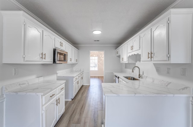 kitchen with sink, white cabinets, light stone counters, light hardwood / wood-style floors, and stainless steel appliances