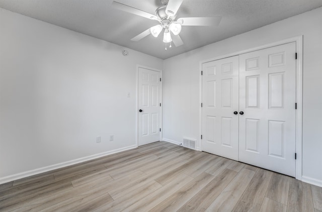 unfurnished bedroom with ceiling fan, a textured ceiling, light wood-type flooring, and a closet