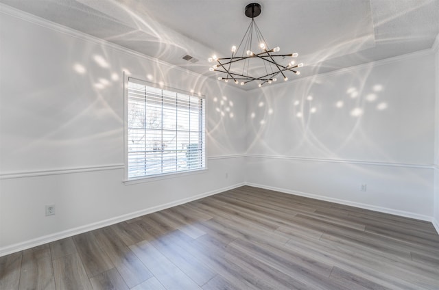 empty room featuring hardwood / wood-style flooring, ornamental molding, and a chandelier