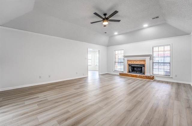 unfurnished living room featuring ceiling fan, light hardwood / wood-style floors, a textured ceiling, a brick fireplace, and vaulted ceiling