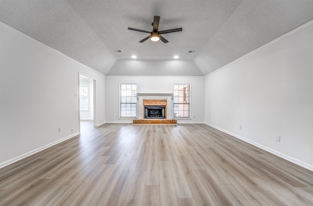 unfurnished living room featuring lofted ceiling, a brick fireplace, light hardwood / wood-style flooring, and a textured ceiling