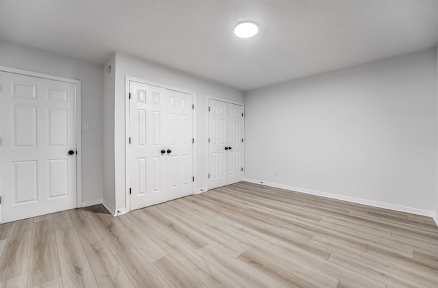 unfurnished bedroom with light wood-type flooring and two closets