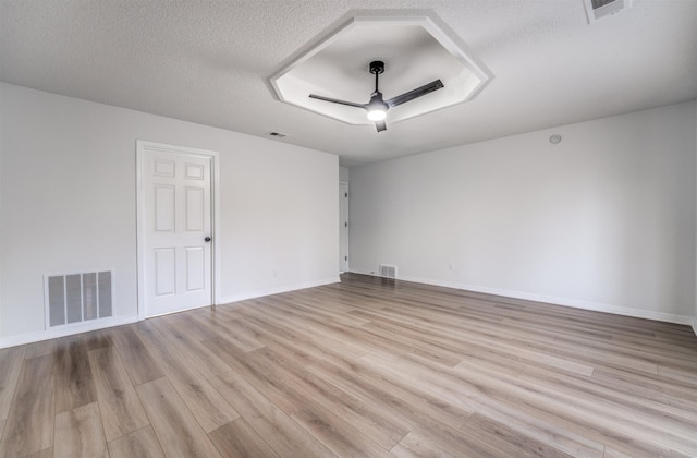 spare room featuring ceiling fan, a raised ceiling, a textured ceiling, and light wood-type flooring