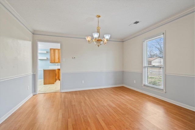 spare room with an inviting chandelier, ornamental molding, a textured ceiling, and light wood-type flooring