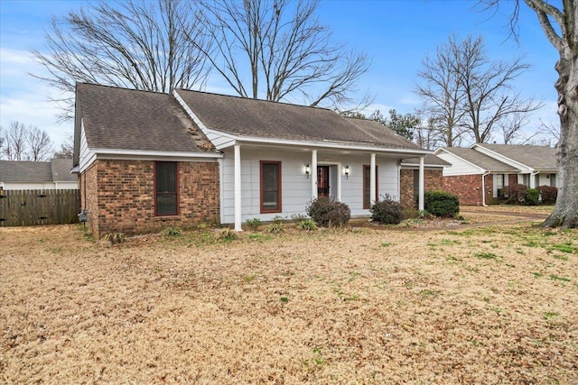 single story home featuring fence, covered porch, roof with shingles, a front yard, and brick siding