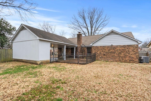 rear view of property with brick siding, fence, central AC, a lawn, and a chimney