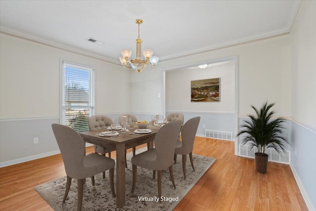 dining space with an inviting chandelier, crown molding, light wood-style floors, and visible vents