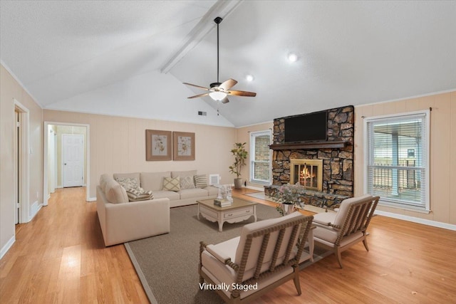 living room with ceiling fan, a fireplace, lofted ceiling with beams, and light wood-style floors