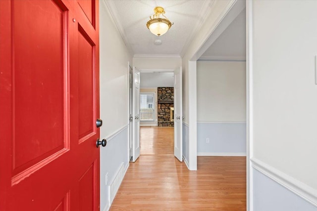 corridor with light wood-style flooring, a textured ceiling, and ornamental molding