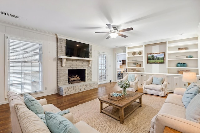 living room featuring ceiling fan, ornamental molding, wood-type flooring, and a fireplace