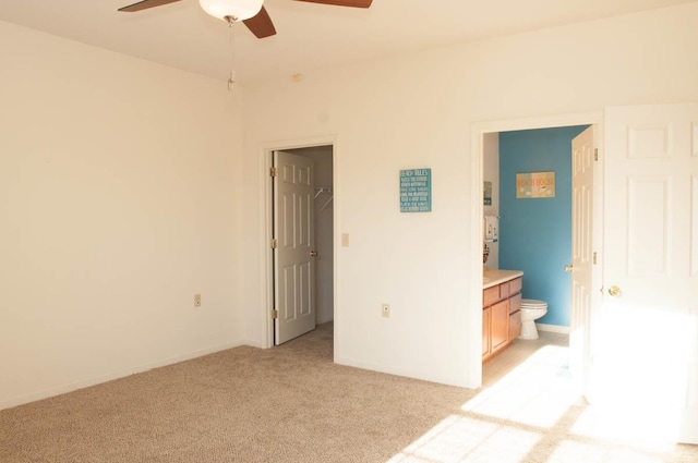 unfurnished bedroom featuring ceiling fan, light colored carpet, ensuite bathroom, and a walk in closet