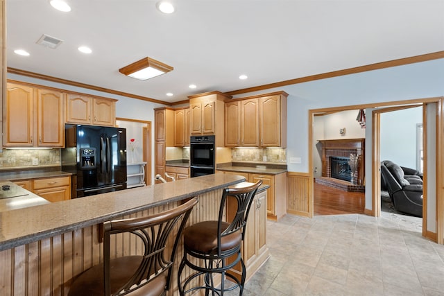 kitchen with crown molding, a breakfast bar area, a fireplace, black appliances, and decorative backsplash