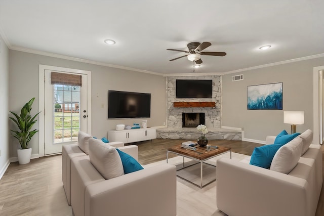 living room with ornamental molding, a stone fireplace, light wood-type flooring, and ceiling fan