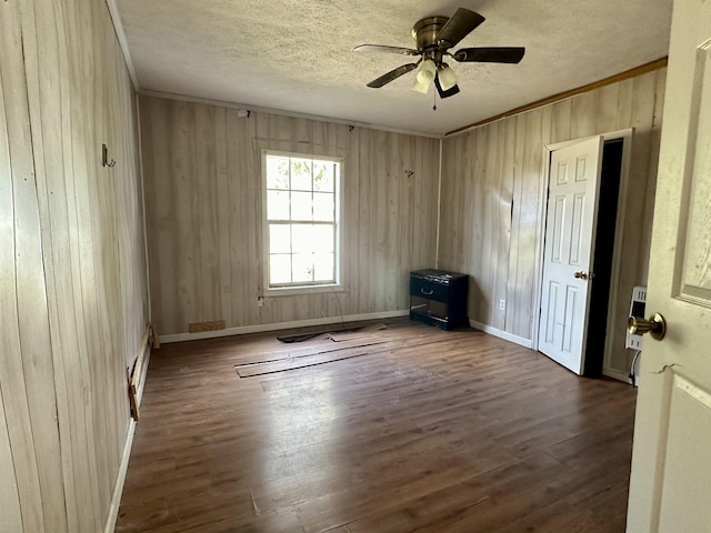 spare room featuring crown molding, a textured ceiling, dark hardwood / wood-style flooring, and wood walls