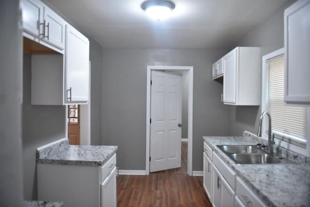 kitchen with white cabinetry, sink, light stone counters, and dark hardwood / wood-style flooring