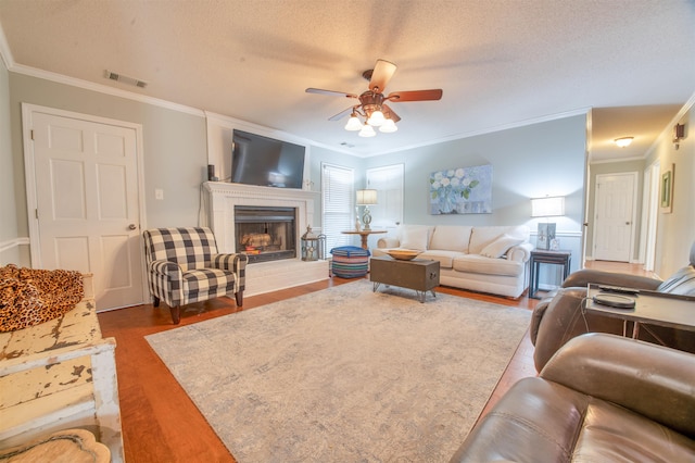 living room featuring hardwood / wood-style flooring, ceiling fan, crown molding, and a textured ceiling