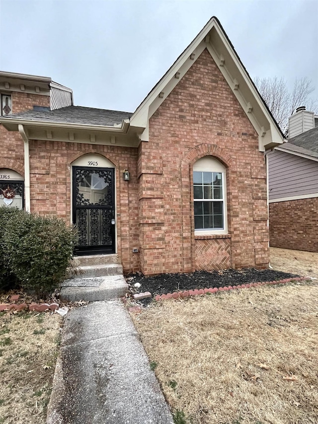 doorway to property with brick siding and roof with shingles