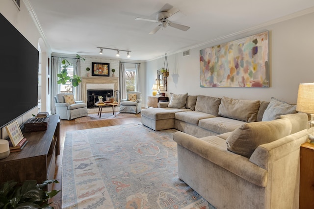 living room with rail lighting, ornamental molding, hardwood / wood-style flooring, ceiling fan, and a fireplace