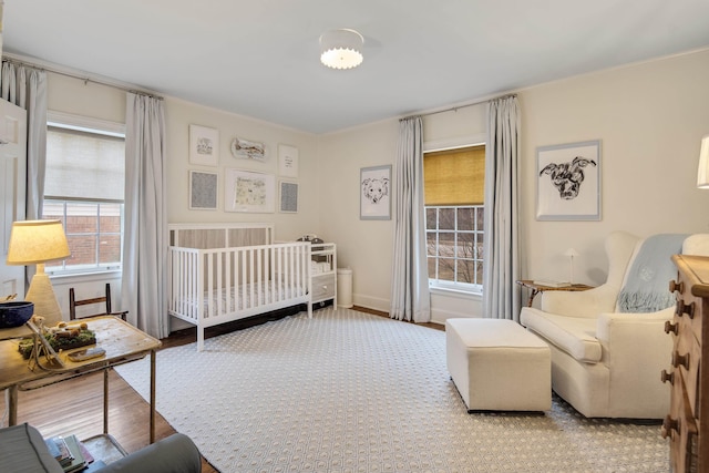 bedroom featuring multiple windows, wood-type flooring, and a nursery area