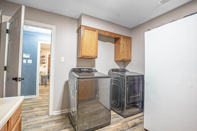 laundry room with cabinets, separate washer and dryer, a textured ceiling, and light wood-type flooring