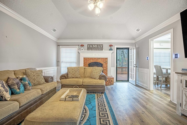 living room with lofted ceiling, hardwood / wood-style flooring, crown molding, a brick fireplace, and a textured ceiling