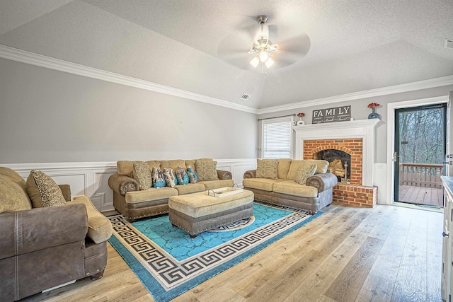 living room featuring a fireplace, lofted ceiling, ornamental molding, light hardwood / wood-style floors, and a textured ceiling