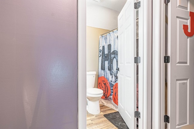 bathroom featuring wood-type flooring, toilet, and curtained shower